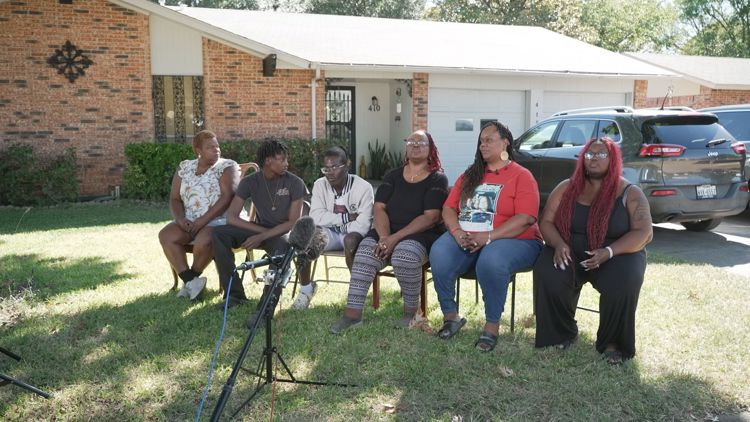 Family members comforting each other at a memorial, seeking justice for a loved one.